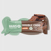 Snímek produktu Hans Energy Bar Double Choc veganská měkká tyčinka s kousky sytě hnědé čokolády a světle šalvějově zeleným obalem s bio etiketou.
