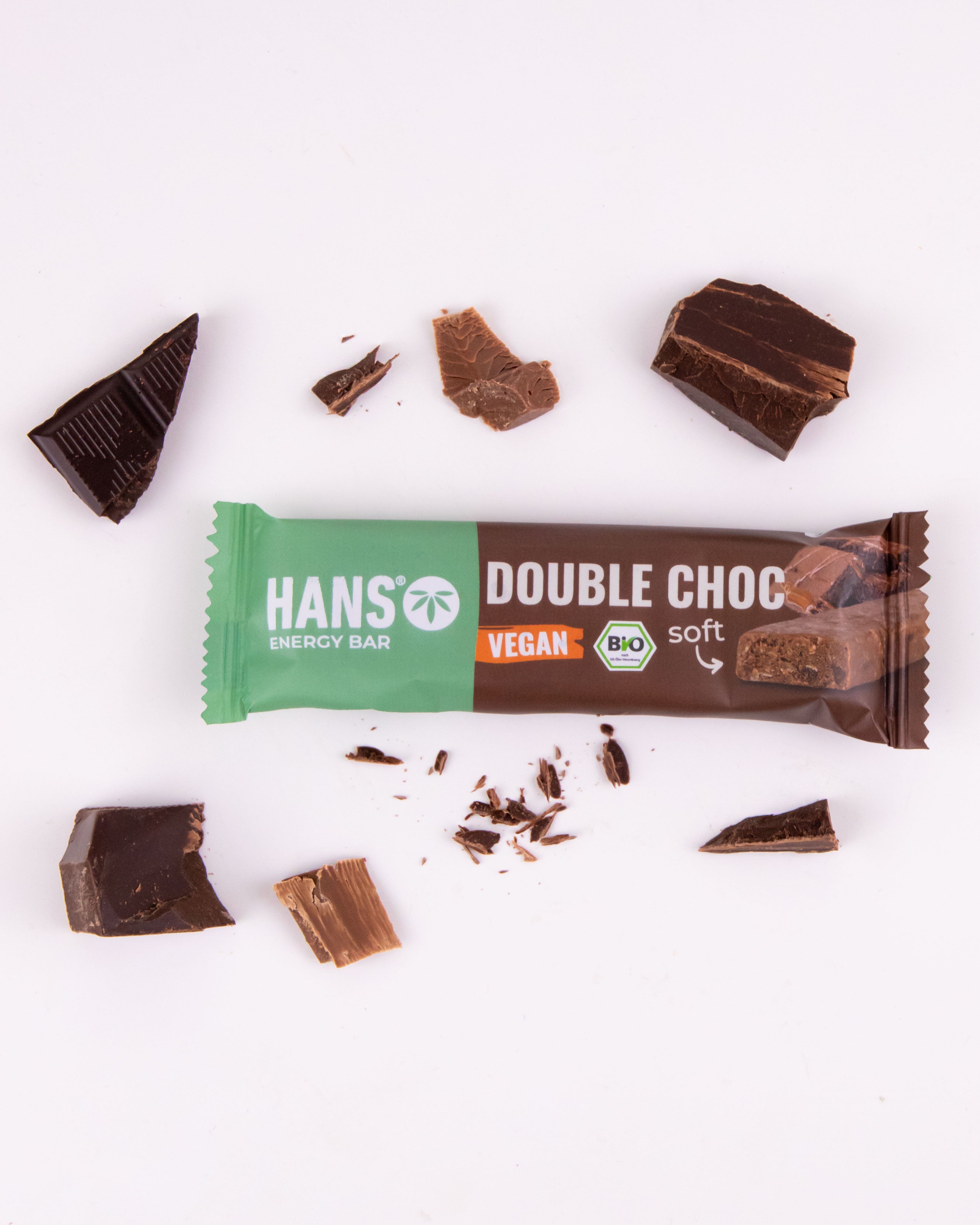 Fotografie veganské měkké čokoládové tyčinky Hans Energy Bar Double Choc a kousků hořké a mléčné čokolády na bílém pozadí