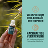 Photograph by unknown artist: hand holding 15% hemp aroma oil with CBD and terpenes in front of a blurred background of hemp leaves, glass bottle with bamboo lid and gold-colored oil are recognizable
