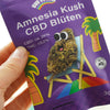 Bud World Amnesia Kush CBD flower packaging features a cartoon hemp flower character on a deck chair in front of palm trees with a rainbow and a quality seal
