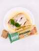Food photography showing a piece of apple strudel with vanilla sauce garnished with mint and a pansy on a white plate alongside a vegan apple strudel energy bar and a separate energy bar
