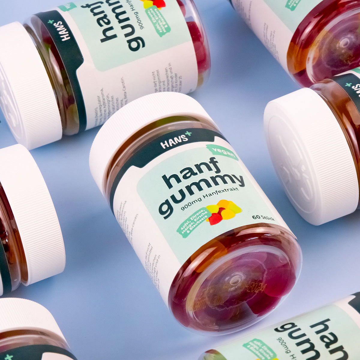 HANS+ vegan hemp gummy, 900mg hemp extract, shows several jars of colorful, fruity hemp gummy bears in apple, lemon, mango, cherry and blueberry on a blue background
