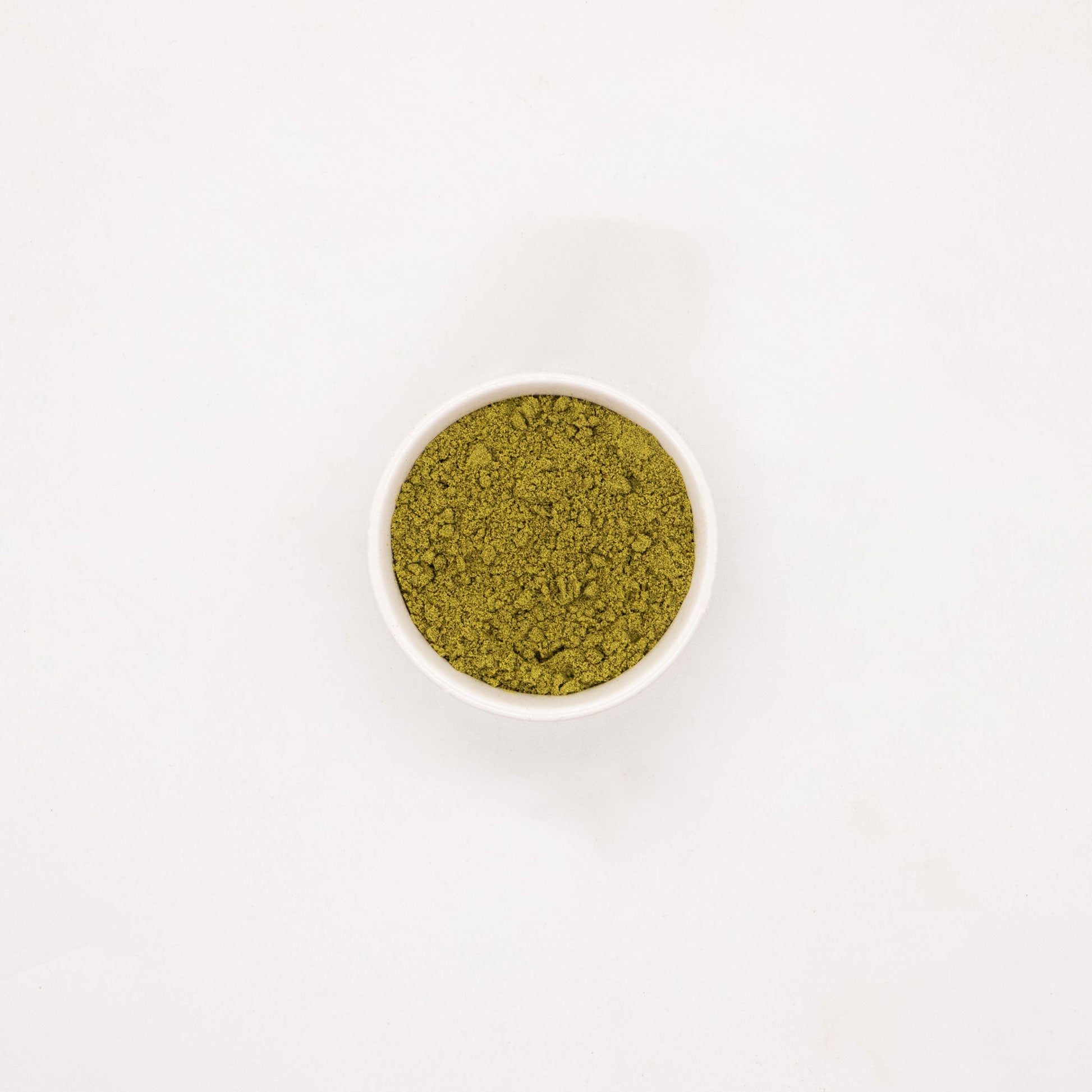 Photography: A small white bowl with olive green, finely ground powder on a white background, reminiscent of damp sand